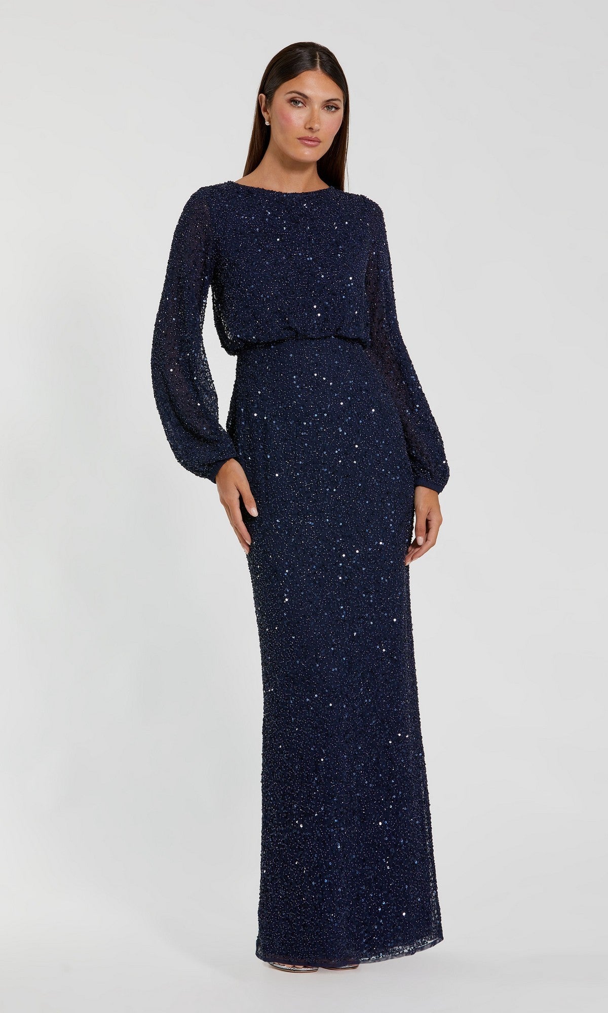 A woman stands against a plain light background, modeling the Mac Duggal 94203 Long Formal Dress in navy—a floor-length, long-sleeve sequin gown with a blouson bodice that perfectly embodies elegant, modest style.